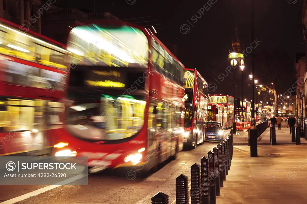 England, London, Westminster. Double decker red London buses travelling through the city at night with Big Ben in the background.