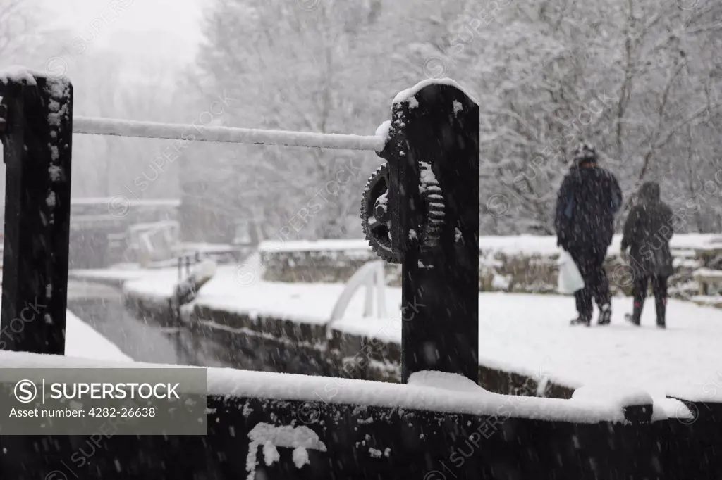 England, Lancashire, Saddleworth. Two people walking along a towpath by the Huddersfield Narrow Canal in the snow.