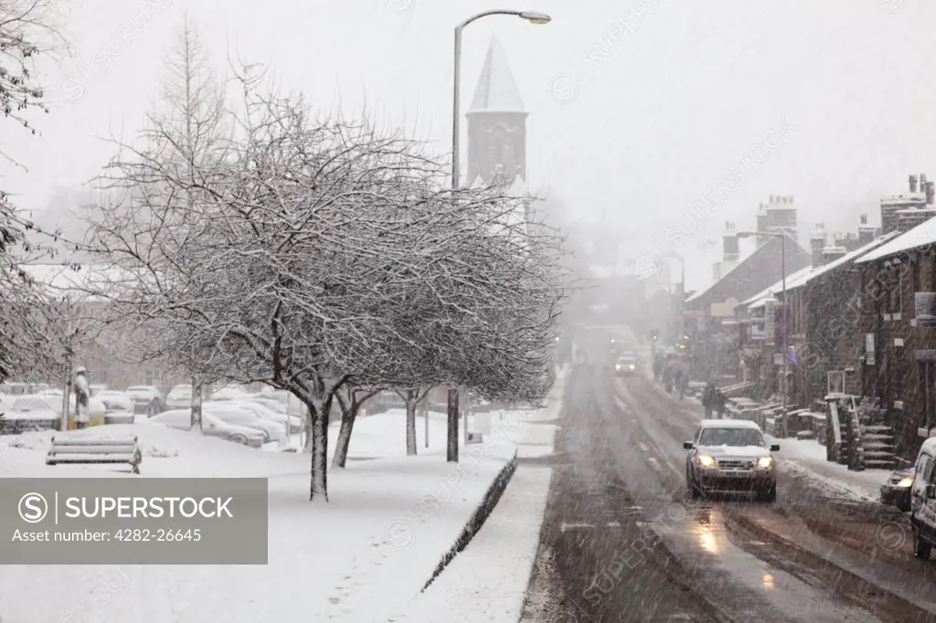 England, Lancashire, Saddleworth. Cars travelling along a road through a village in heavy snow.