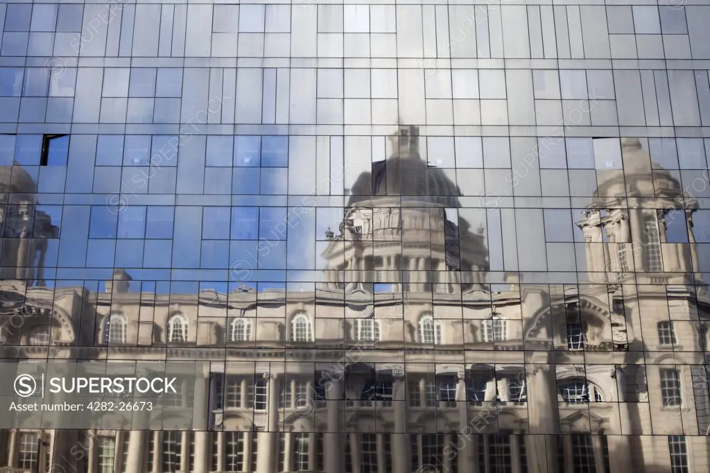 England, Merseyside, Liverpool. The Port of Liverpool Building reflected in the glass cladding of a modern new building.