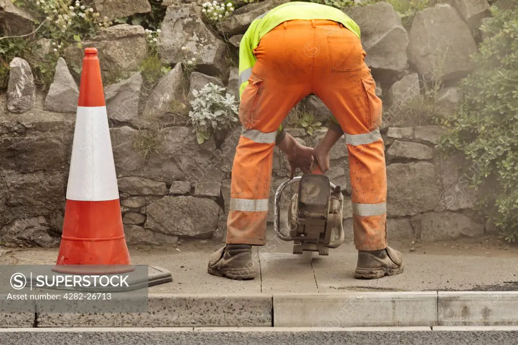 England, Somerset, Weston-super-Mare. Workman bending over to cut a paving slab.