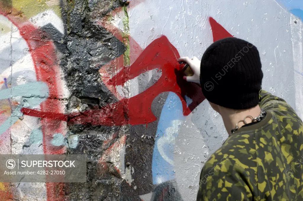 England, Sussex, Brighton. A young man sprays graffiti on a wall in Brighton. Areas of the south coast city have been set aside for graffiti artists in an attempt to reduce illegal graffiti and tagging.