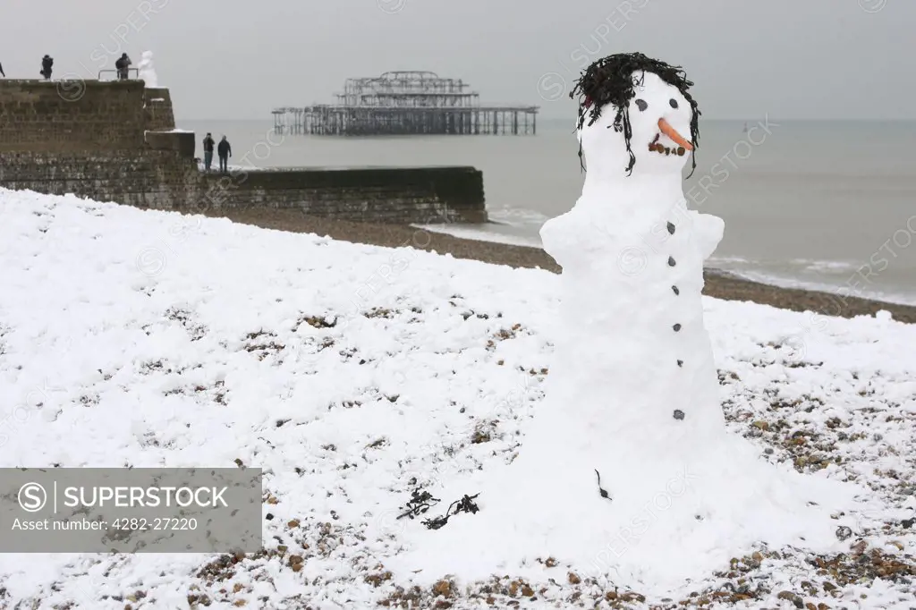 England, Somerset, Weston-Super-Mare. Snowman along the beachfront and in the distance the recently ruined Grand Pier in Weston-Super-Mare.