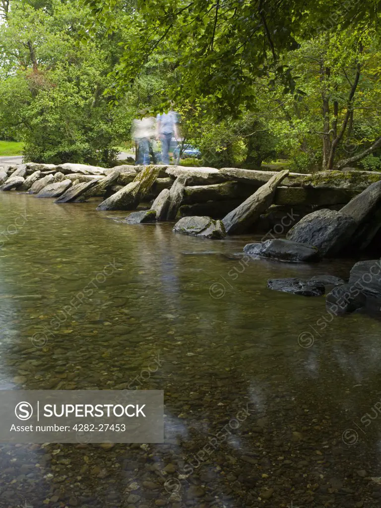 England, Somerset, Winsford. People crossing the River Barle over Tarr Steps, an ancient clapper bridge in Exmoor National Park.
