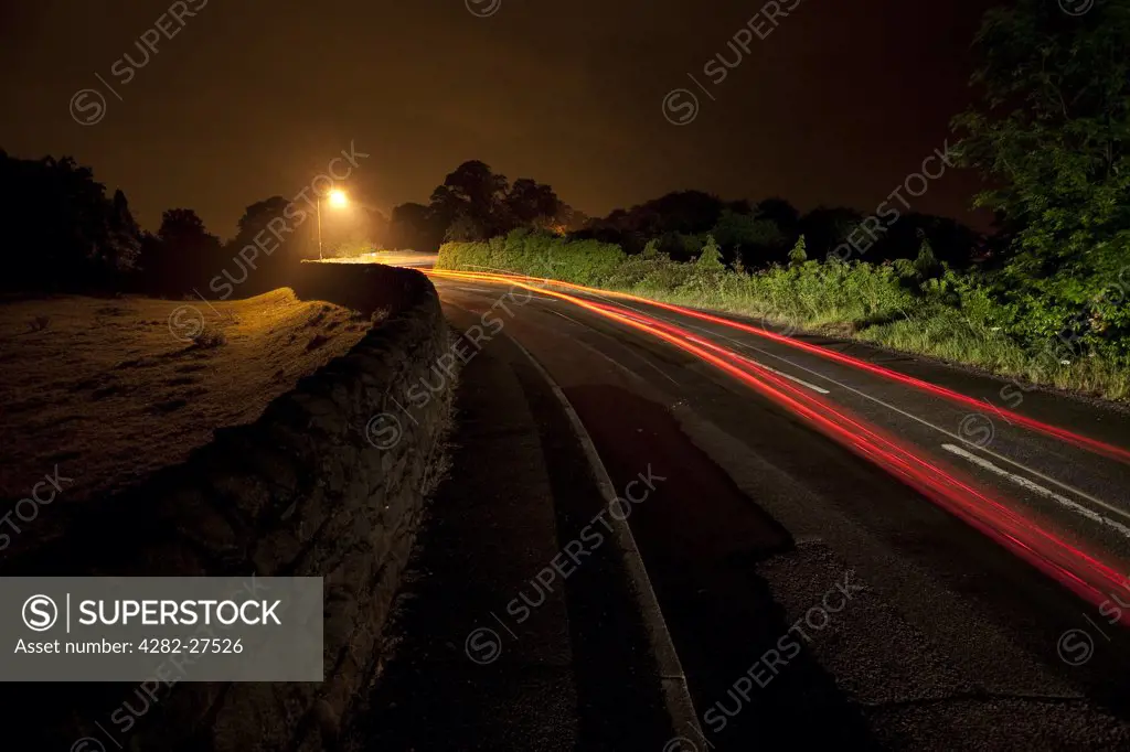 England, Leicestershire, Loughborough. Light trail from a car travelling along a rural road at night.