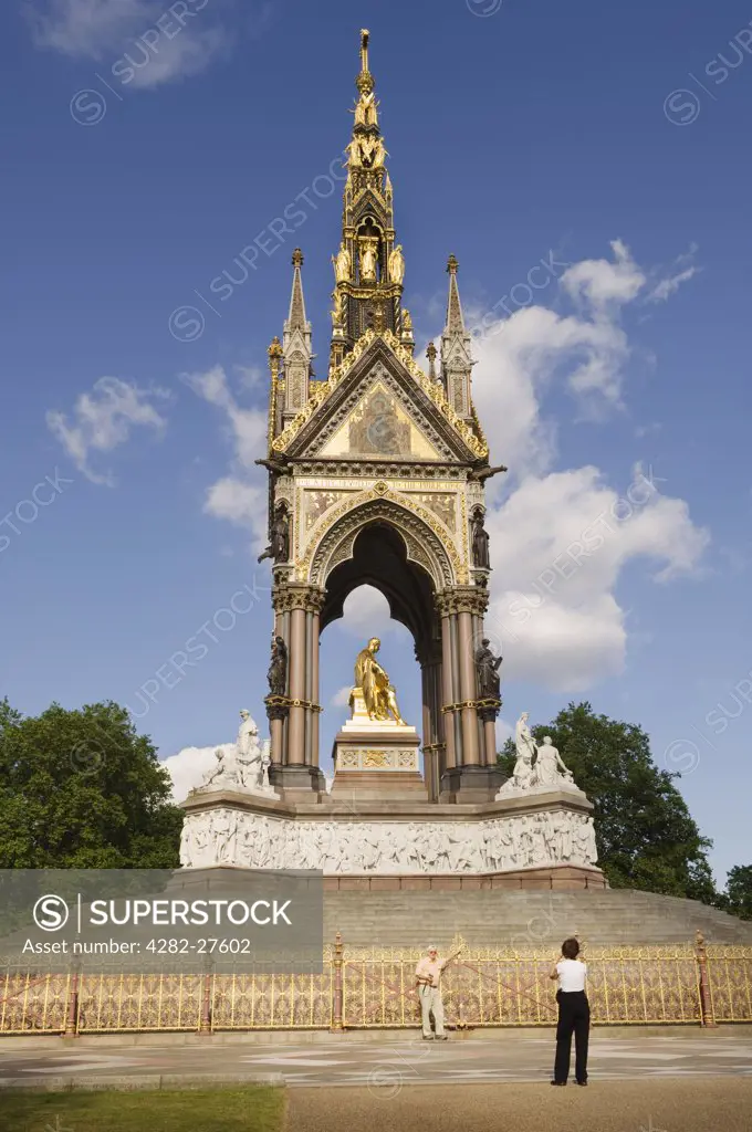 England, London, Hyde Park. A tourist standing for a photograph in front of the Albert Memorial in Hyde Park.