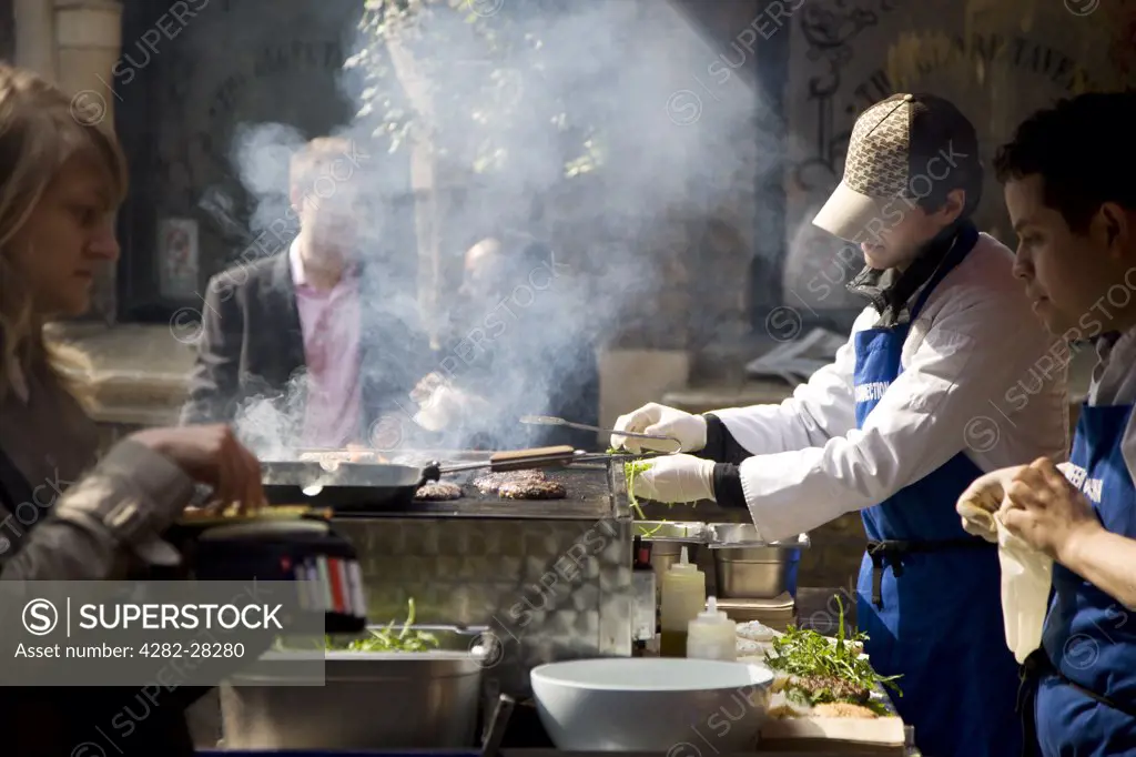 England, London, Borough Market. Customers watch as burgers are put onto a griddle in Borough Market.