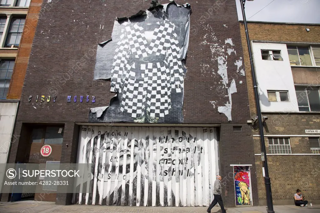 England, London, Shoreditch. A man walking past the front of Cordy House (a venue with 20,000 square feet of event space) displaying Graffiti and a large torn poster in Curtain Road.