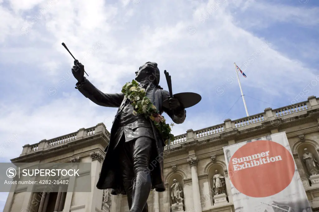 England, London, Piccadilly. A sculpture of Sir Joshua Reynolds outside the Royal Academy of Arts in front of a large banner advertising the annual summer exhibition.