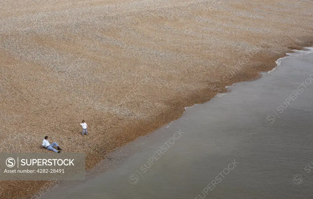 England, East Sussex, Brighton. A father and son on a deserted pebble beach.