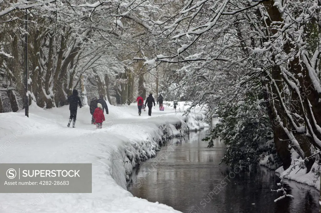 England, Gloucestershire, South Cerney. People walking through thick snow along Bow Wow, a lane running alongside the River Churn in winter.
