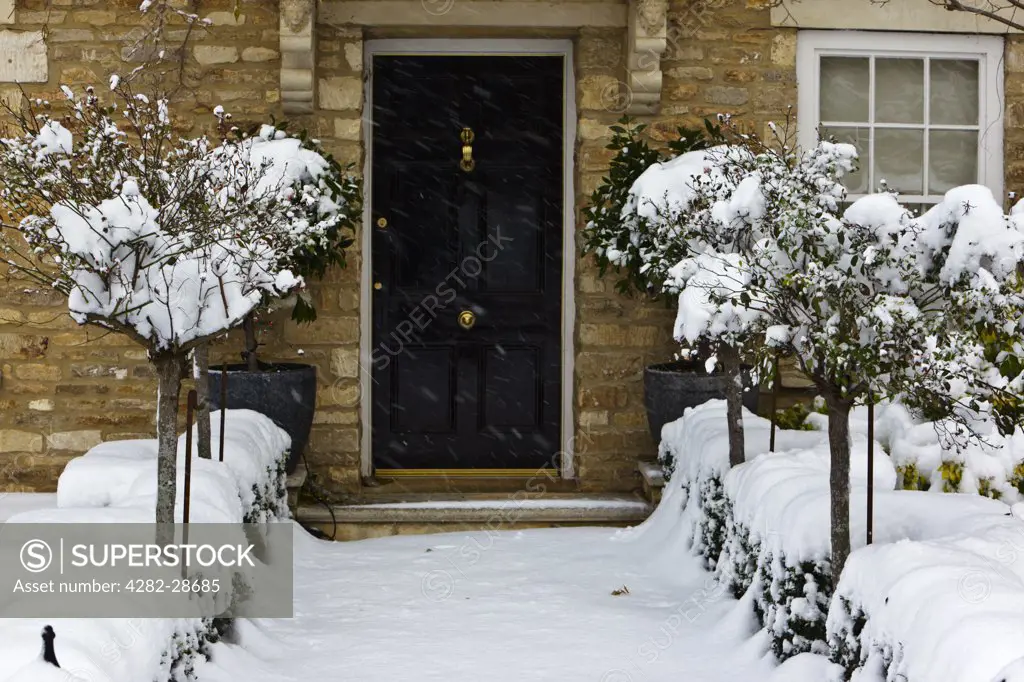 England, Gloucestershire, South Cerney. A snow covered path leading up to a black front door of a stone built house in the Cotswolds.