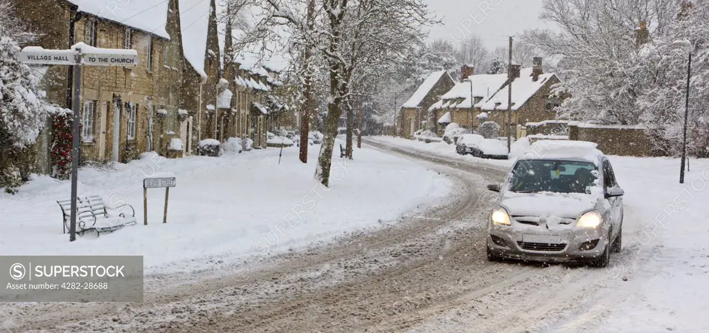 England, Gloucestershire, South Cerney. A car struggling through falling snow on Silver Street in the Cotswolds village of South Cerney.