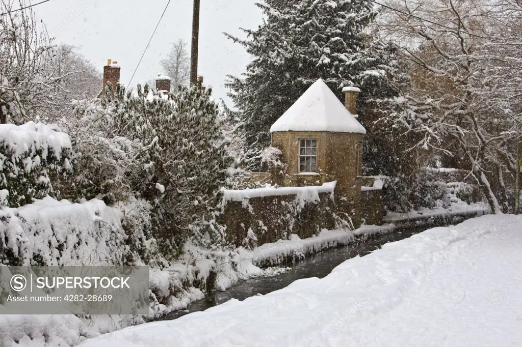 England, Gloucestershire, South Cerney. Thick snow covering the oddly named 'Bow Wow', a lane in the Cotswold village of South Cerney running between the River Churn and a mill stream.