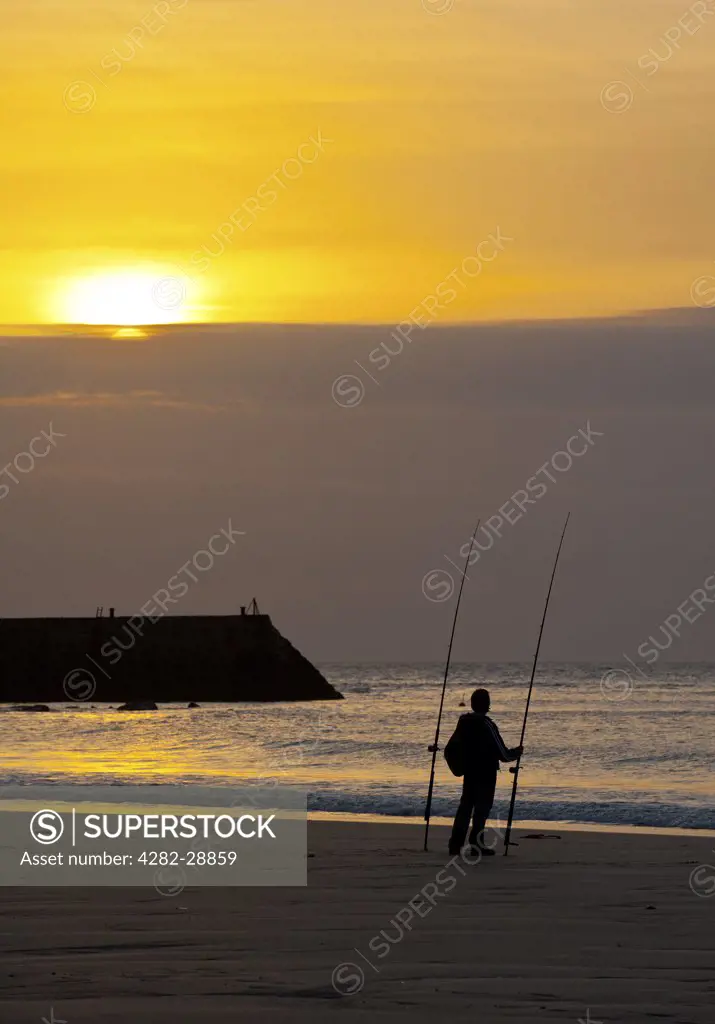 England, Cornwall, Sennen. An angler on Sennen beach at sunset.