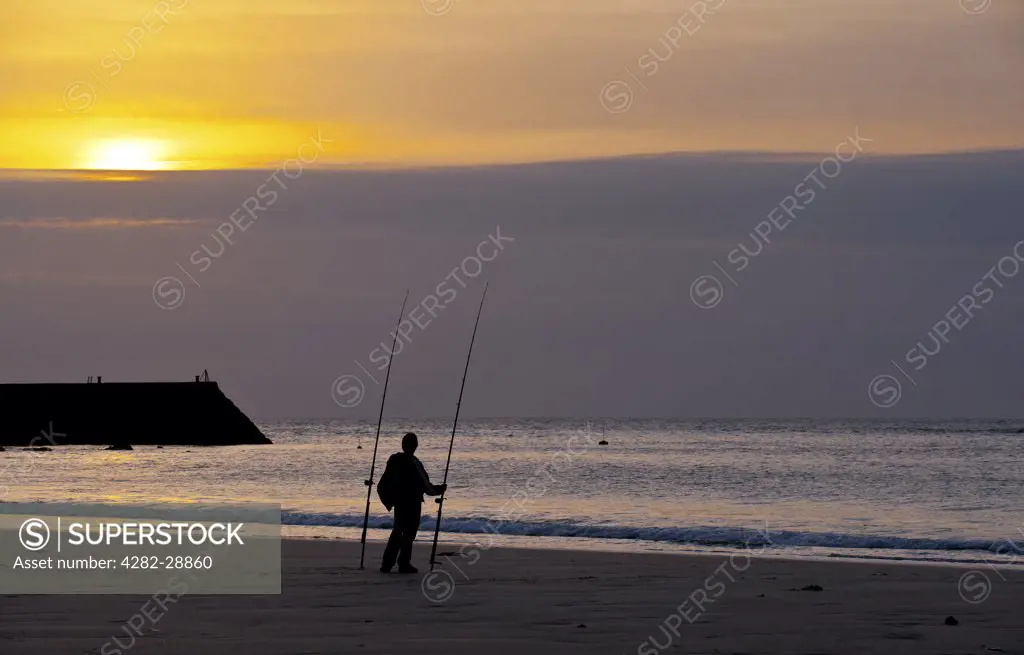 England, Cornwall, Sennen. An angler on Sennen beach at sunset.