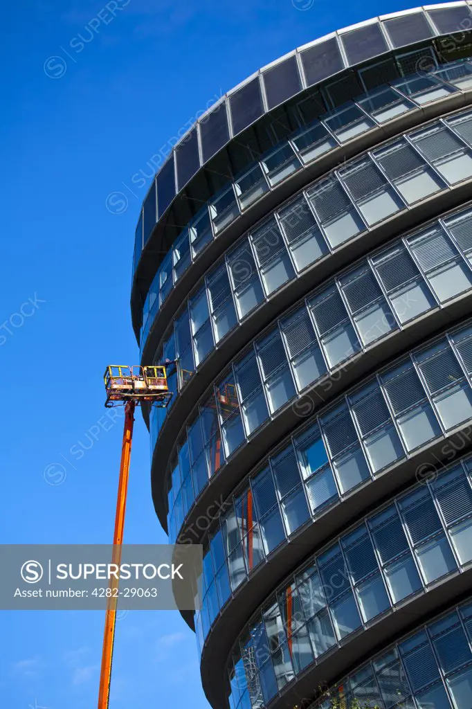 England, London, Southwark. A workman performing maintenance from a cherry picker on a window of City Hall, home of the Greater London Authority (GLA) comprising of the Mayor of London and London Assembly.