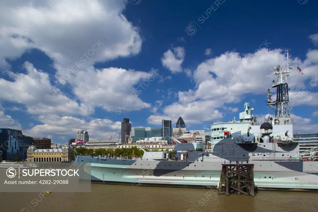 England, London, Southwark. HMS Belfast, originally a Royal Navy light cruiser, permanently moored in London on the River Thames with the City of London and the Gherkin in the background.