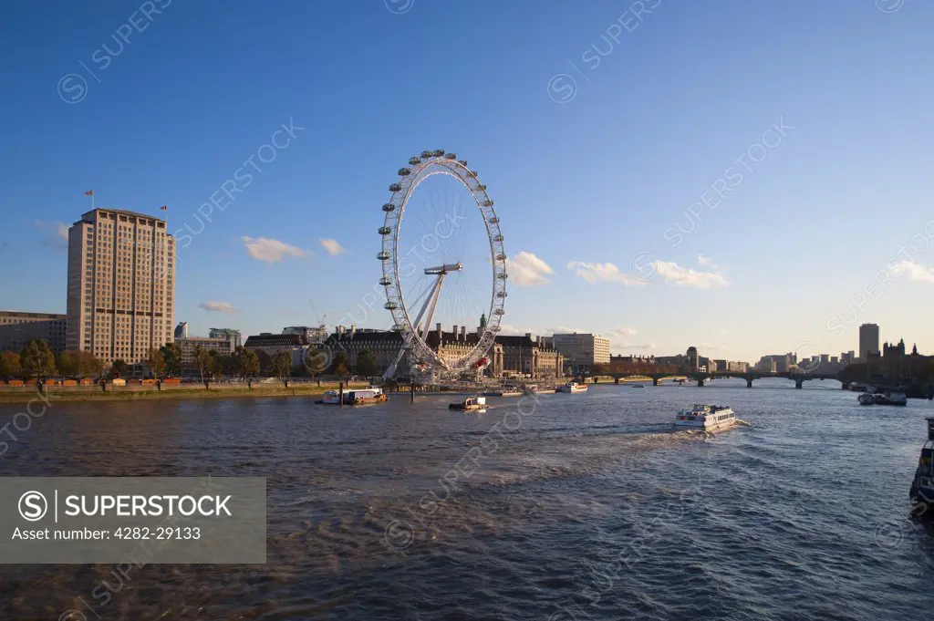 England, London, South Bank. Autumn evening sunlight on Shell Centre and the iconic London Eye with a passing riverboat on the river Thames.