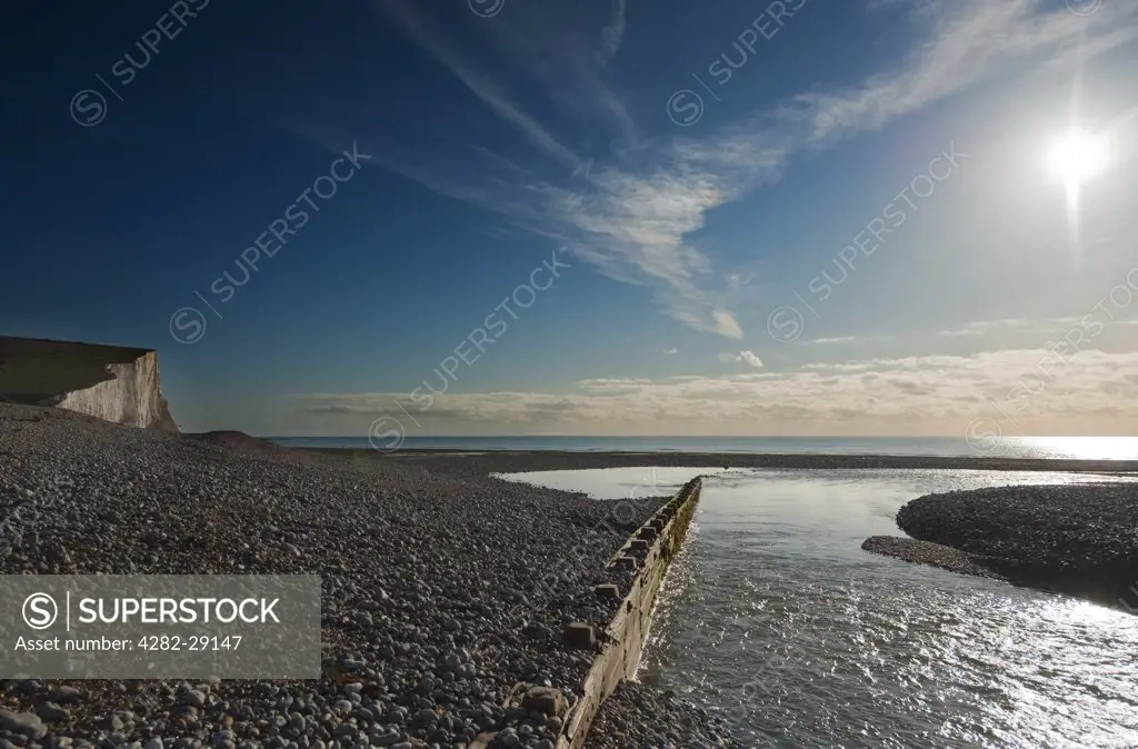 England, East Sussex, Cuckmere Haven. The River Cuckmere entering the sea between wooden levees and shingle banks at Cuckmere Haven.