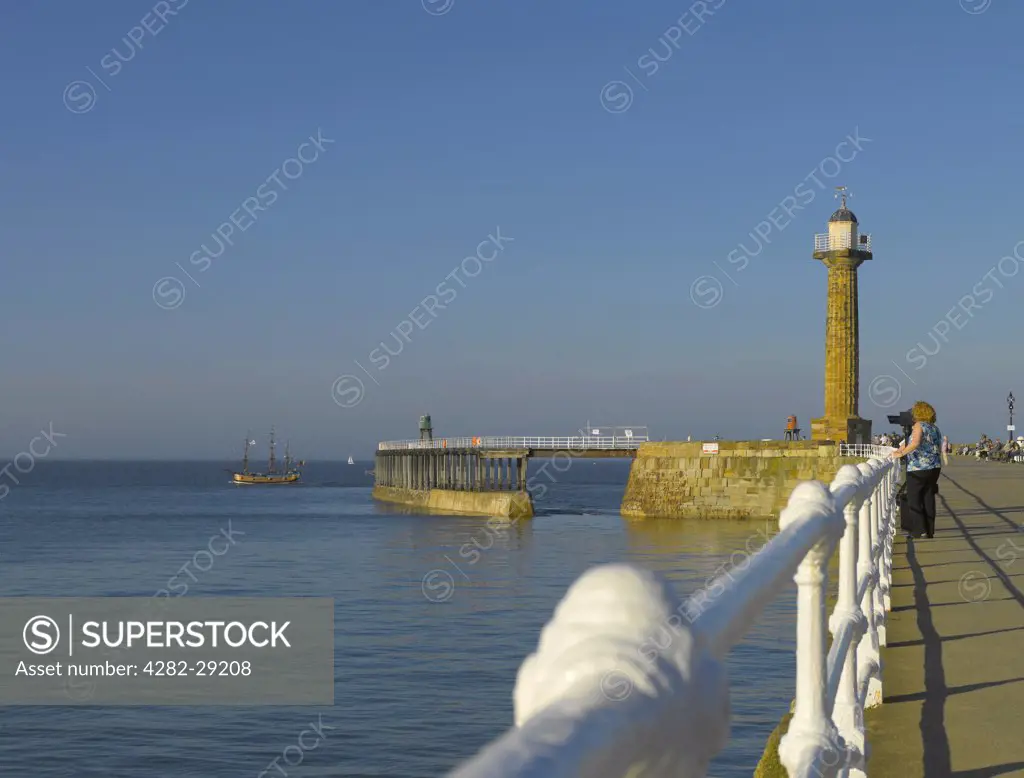 England, North Yorkshire, Whitby. Tourists looking out to sea from the west pier at Whitby with the 19th century west pier lighthouse in the background.