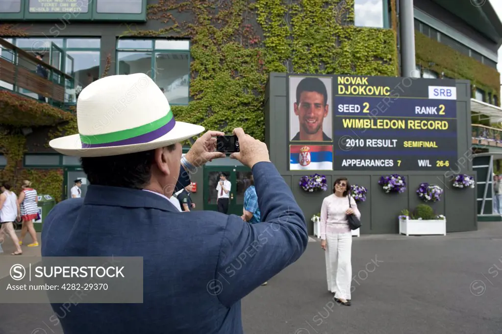 England, London, Wimbledon. A man taking a photograph of a woman standing in front of a scoreboard outside centre court at the 2011 Wimbledon Tennis Championships.