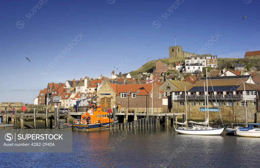 England, North Yorkshire, Whitby. Whitby lifeboat moored outside Whitby Lifeboat Station below St Mary's Church on the hill above.
