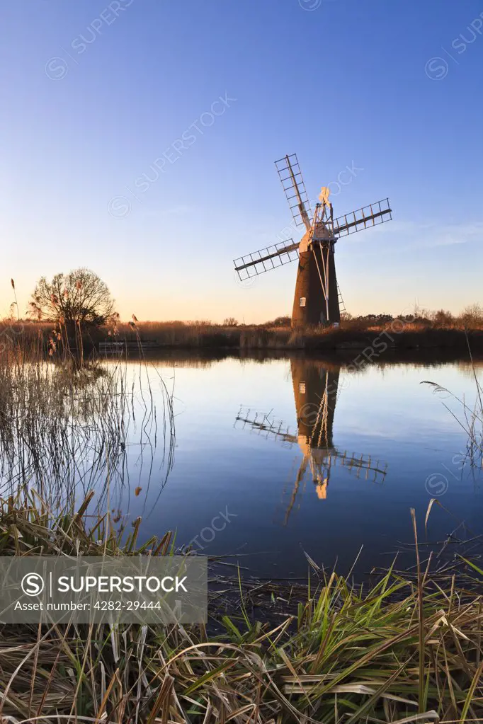 England, Norfolk, Ludham. Turf Fen wind pump reflected in still water at How Hill on a winters evening.