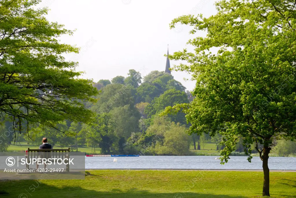 England, London, Wimbledon. A man sitting on a park bench looking out over a lake in Wimbledon Park.