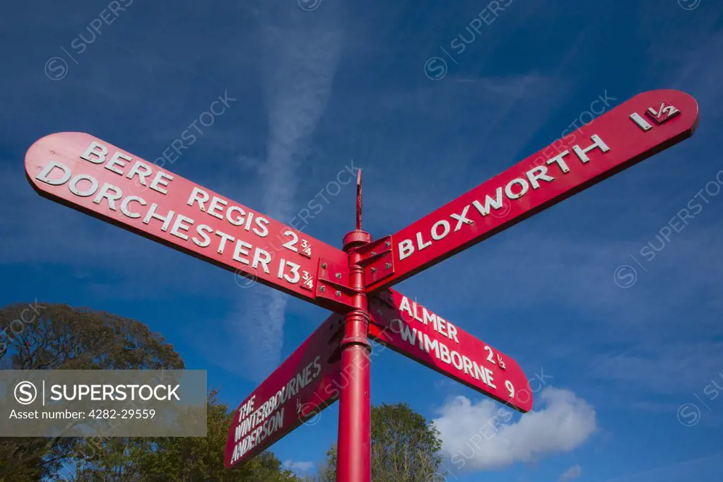 England, Dorset, Bere Regis. Bright red directional road sign at a crossroads.