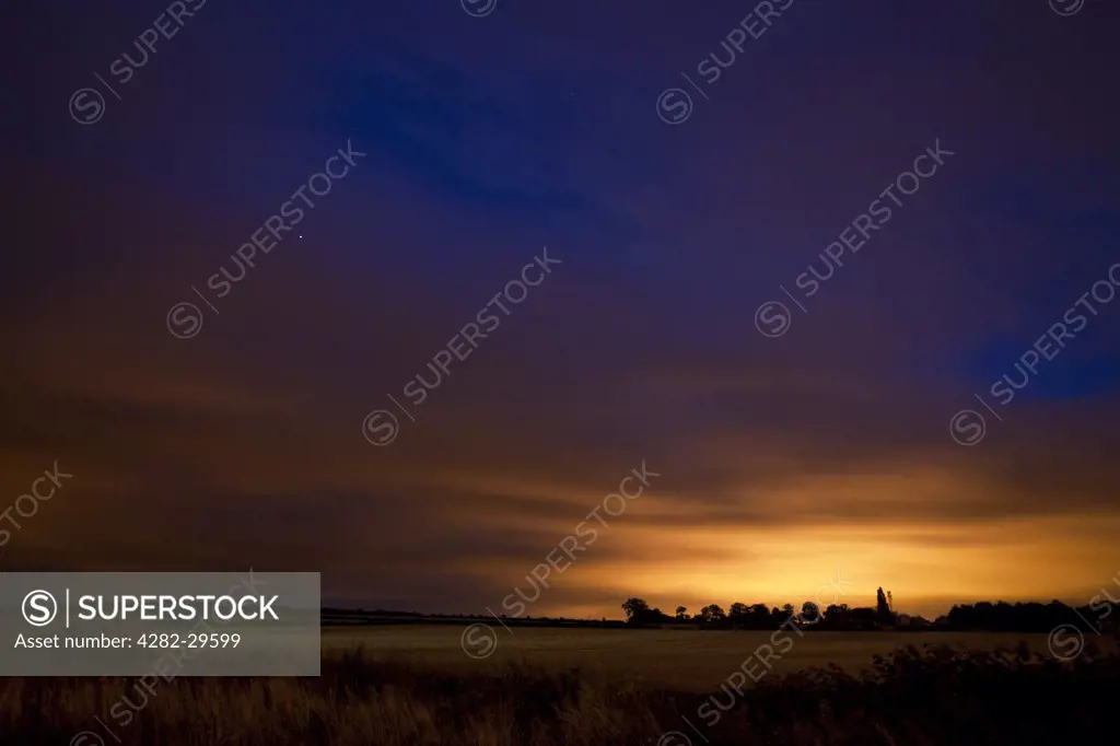 England, Leicestershire, Loughborough. Twilight over a rural field, with distant streetlights reflecting off low clouds.