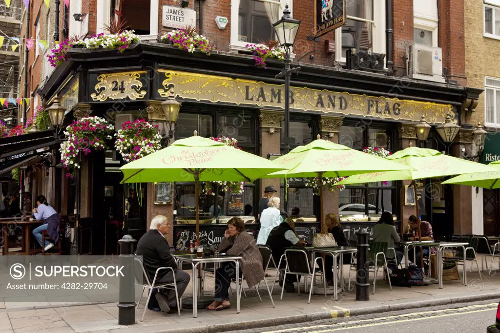 England, London, Marylebone. People sitting under parasols outside the Lamb and Flag pub in James Street.