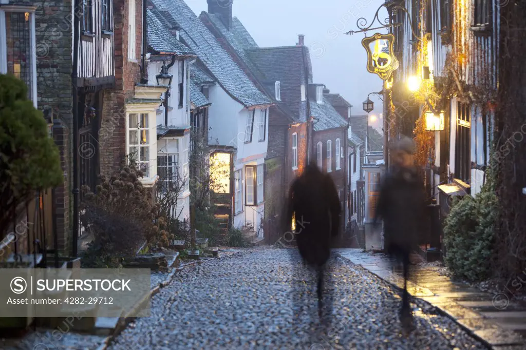 England, East Sussex, Rye. Two people walking up a traditional cobbled street past the Mermaid Inn in Rye.