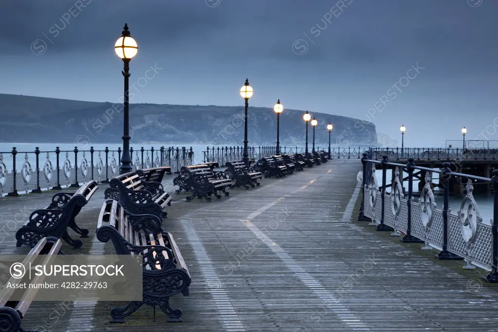 England, Dorset, Swanage. Benches under lamps along Swanage pier at twilight.