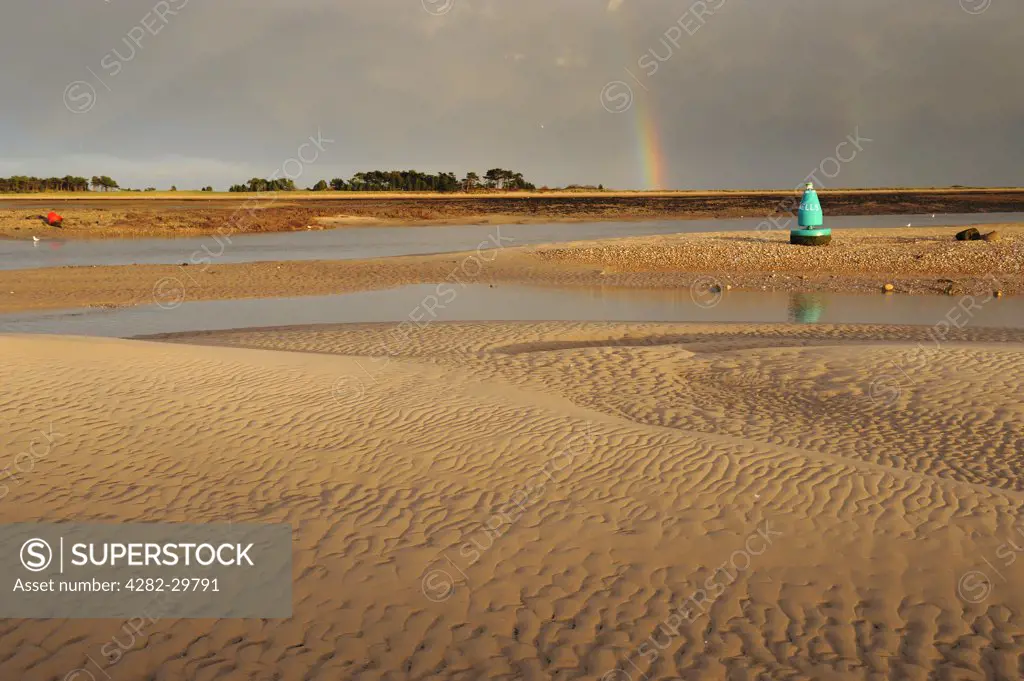 England, Norfolk, Wells-next-the-Sea. Rainbow over the 'East Hills' off Wells-next-the-sea, with sandbanks in the foreground.