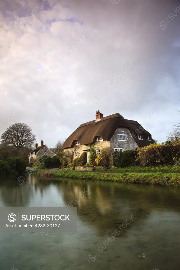 England, Wiltshire, Sherrington. View across a pond towards thatched cottages at Sherrington.