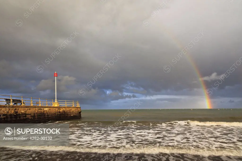 England, Dorset, Swanage. Rainbow over the sea at Swanage with the Banjo Jetty in the foreground.