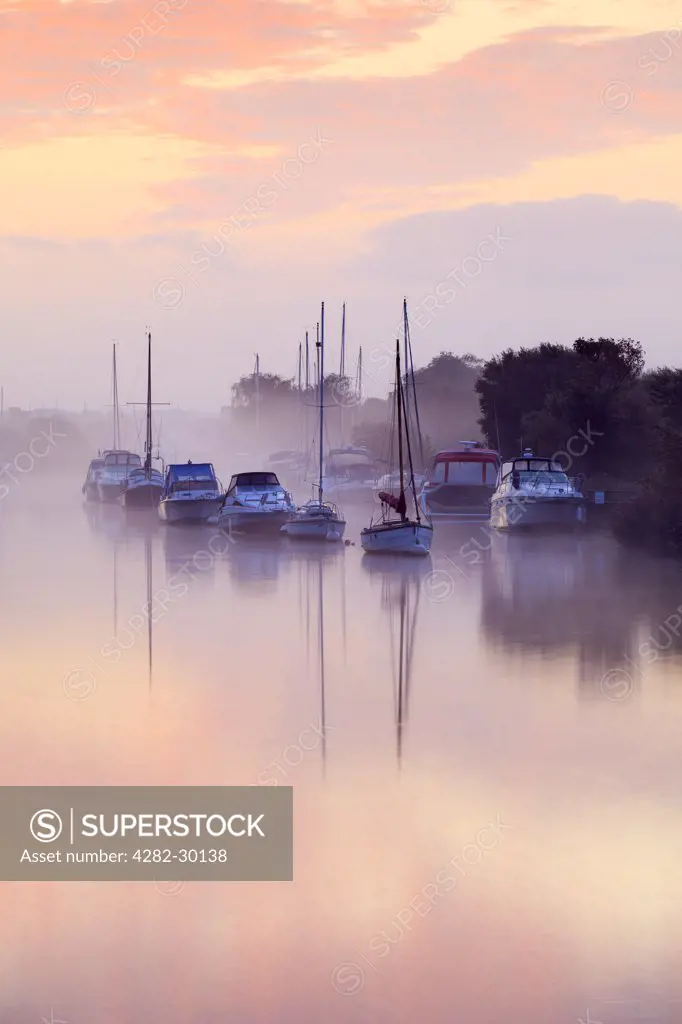 England, Dorset, Wareham. Early morning mist lingering over small pleasure boats moored on the River Frome at Wareham Quay.