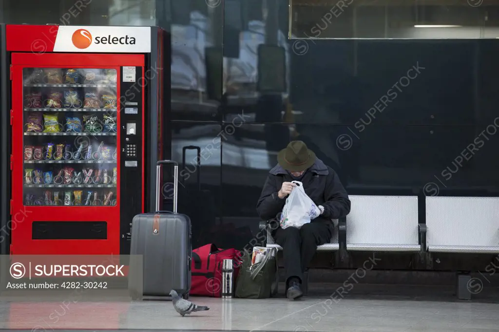 England, Tyne and Wear, Newcastle upon Tyne. A passenger sitting with holdalls next to a vending machine on a platform at Newcastle Central Station.