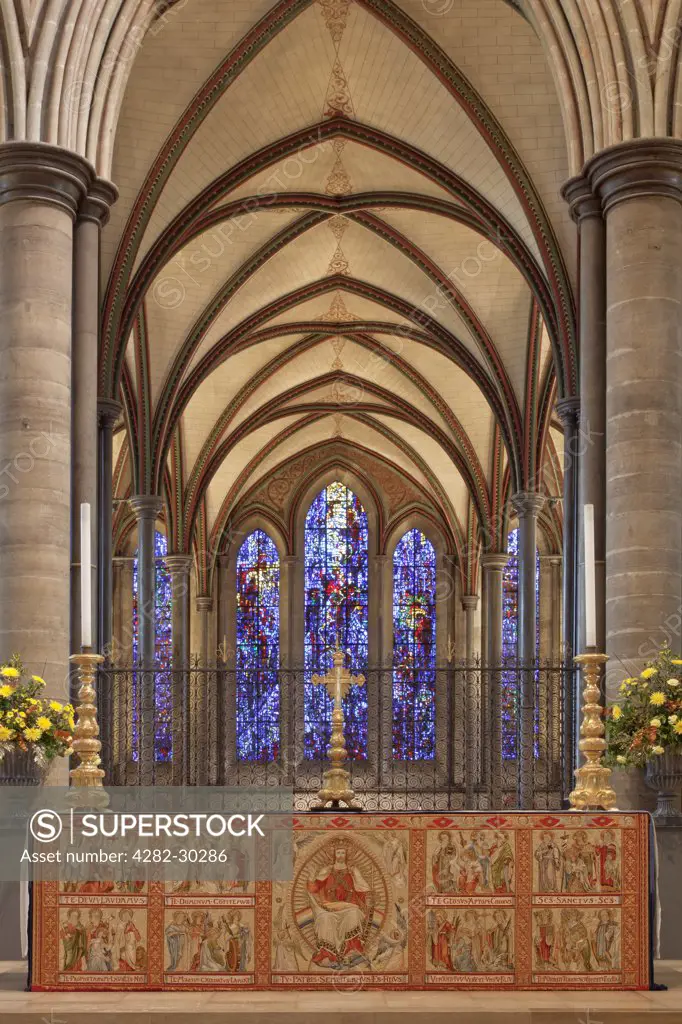 England, Wiltshire, Salisbury. High Altar in Salisbury Cathedral with embroidered cloth and the stained glass window of Trinity Chapel in the background.