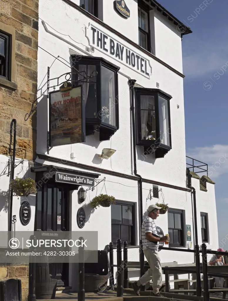 England, North Yorkshire, Robin Hood's Bay. A man carrying drinks outside of The Bay Hotel in Robin Hood's Bay, once the busiest smuggling community on the Yorkshire coast.