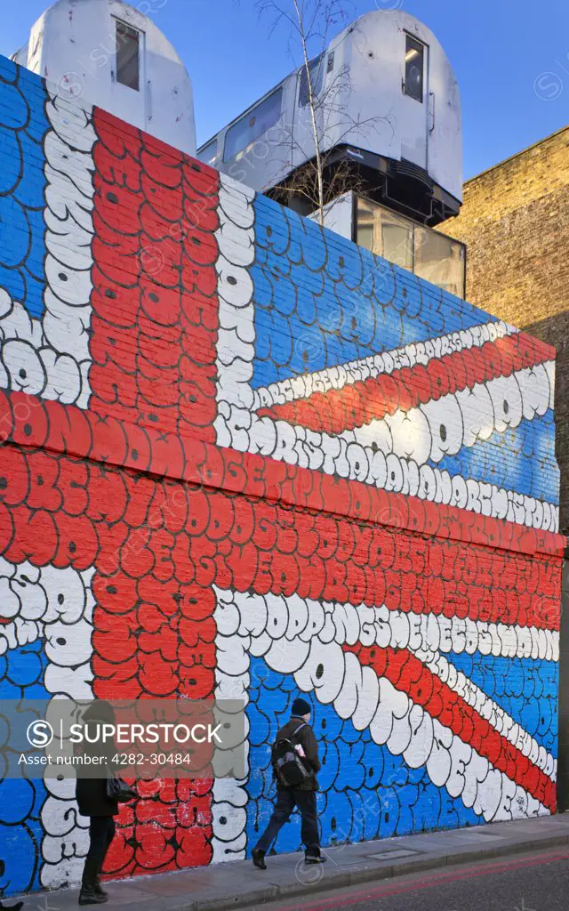 England, London, Shoreditch. Londoners walk to work past an image of the Union flag painted on a wall in bubble letters in the East End of London.
