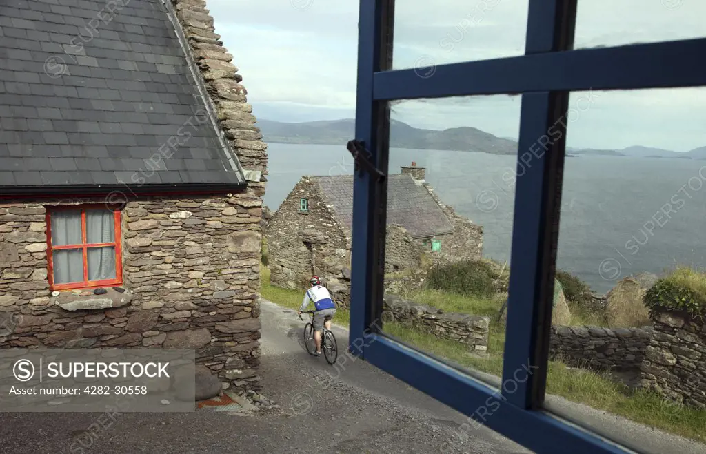Republic of Ireland, County Kerry, Ballinskelligs. Cyclist in Cill Rialaig, an 18th century deserted village destined for demolition until rescued by arts patron Noelle Campbell Sharpe and restored as an artists retreat where artists may stay free of charge.