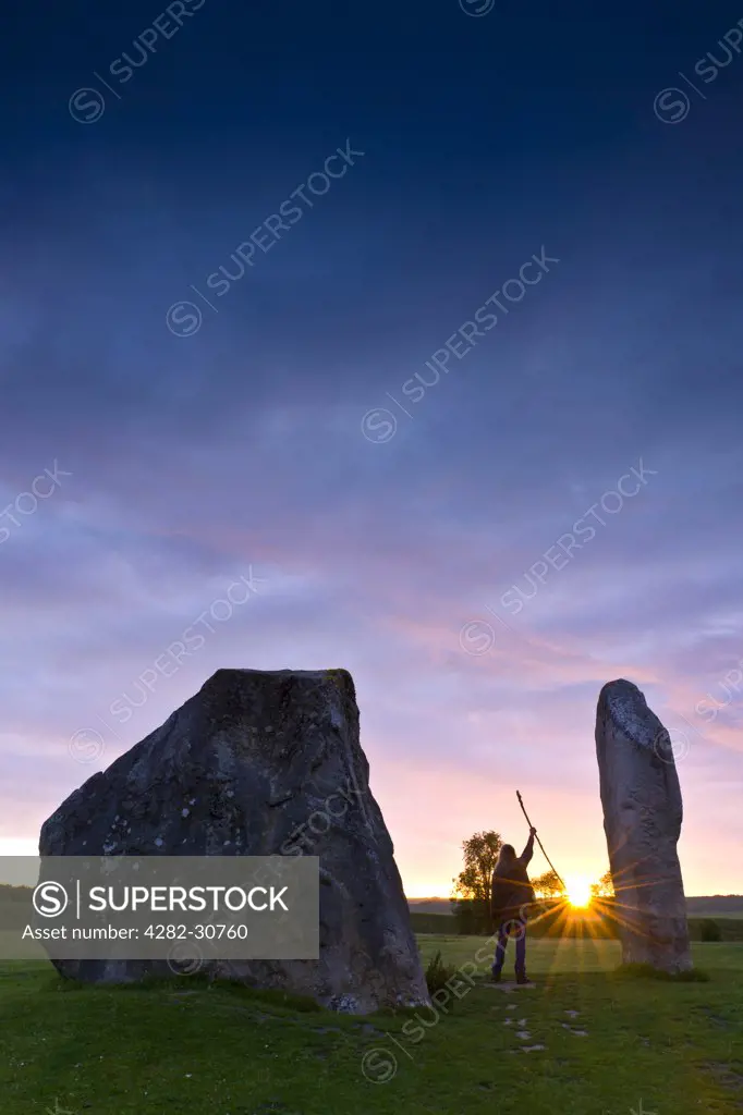 England, Wiltshire, Avebury. Person holding up a staff greeting the sunrise during the summer solstice at the Avebury ring, the oldest stone ring known to be in existence in the world.