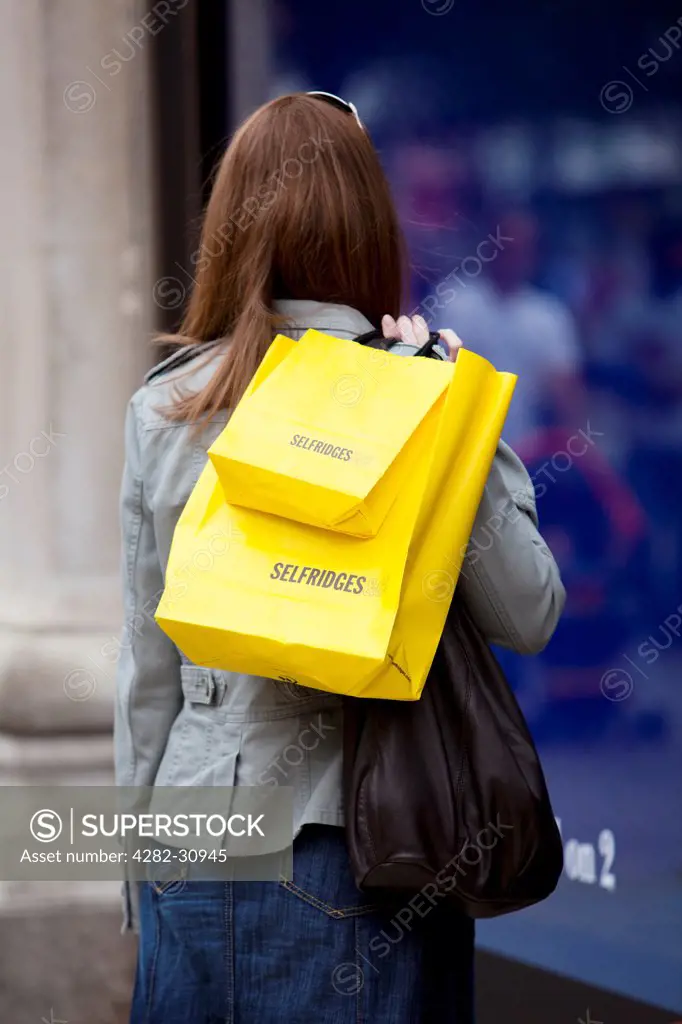 England, London, Oxford Street. A young lady on Oxford Street with bright yellow shopping bags from Selfridges.