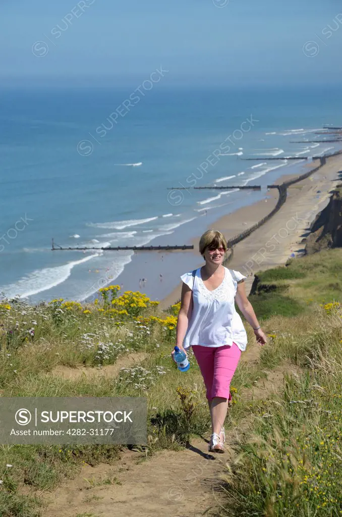 England, Norfolk, Beeston Bump. A woman walking the North Norfolk coastal cliff top path at Beeston Bump in summer.