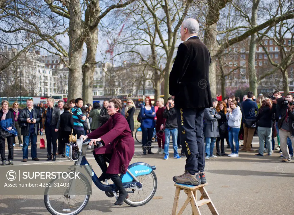England, London, Hyde Park. A woman riding a bicycle past a man precahing at Speakers Corner in London.