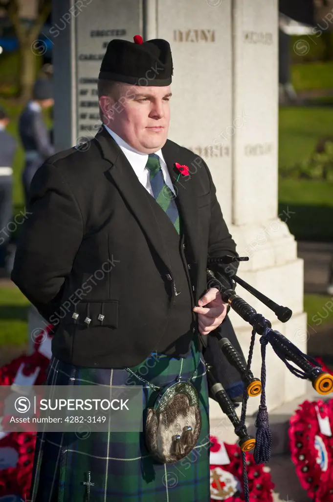 Scotland, South Lanarkshire, Carluke. A piper standing to attention in respectful silence by the war memorial on Remembrance Sunday in the Scottish town of Carluke.