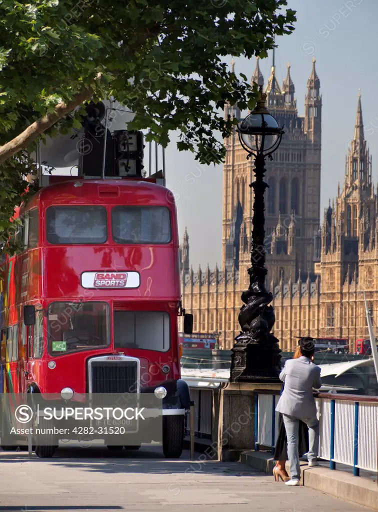 England, London, Waterloo Embankment. A traditional London bus parked on Waterloo Embankment with the Houses of Parliament in the background.