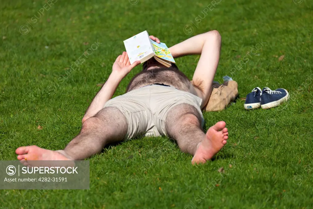 England, Oxfordshire, Oxford. A man reading on the grass on a spring day at Christ Church College Meadows in Oxford.